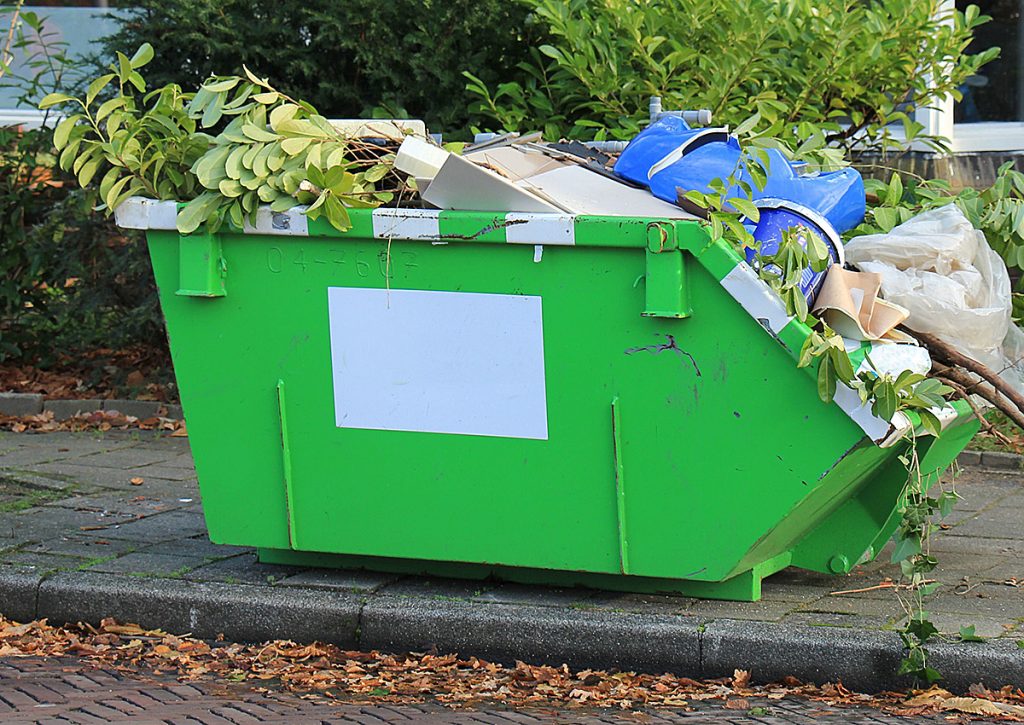 A green skip bin located outside which is full of rubbish