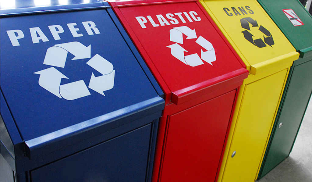 Colour-coded recycling bins labelled for paper, plastic and cans, promoting the separation of recyclable materials.